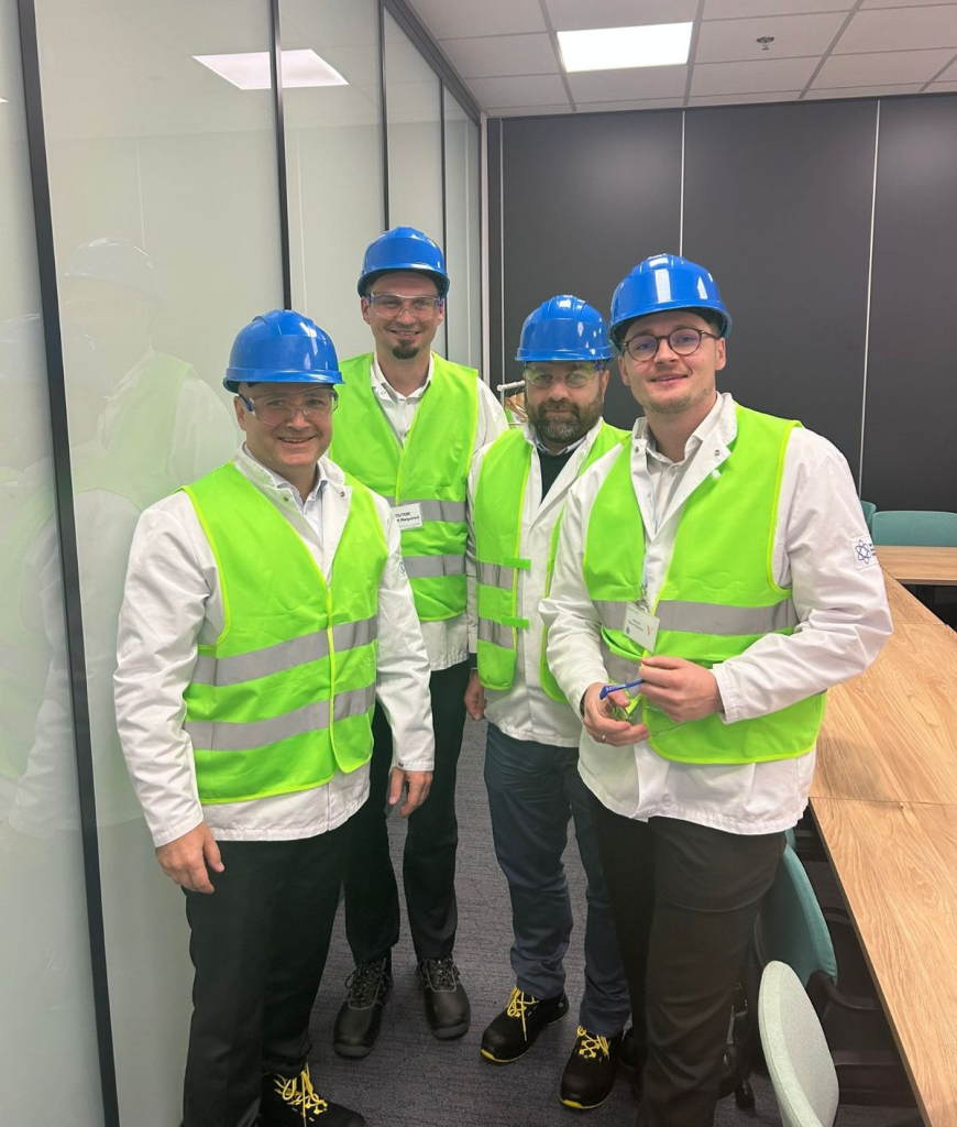 From left to right: Jakub Orczyk, Łukasz Borzęcki, Wojciech Bednarczyk, and Mariusz Mrowiec wearing safety helmets, high-visibility vests, and protective clothing during an industrial facility visit, representing VM.pl in a production environment.