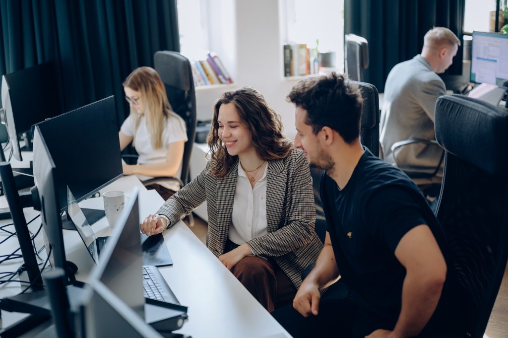 Photo of VM.PL employees collaborating at computer workstations in the office. Team members are working together on project development and daily tasks.